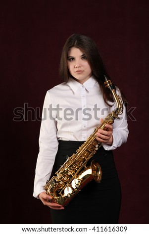 Young girl with saxophone in studio on dark background