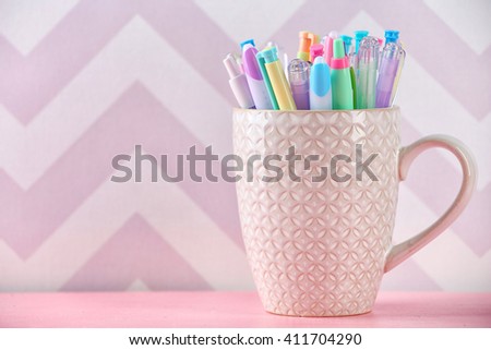 Pens in ceramic cup, pencils and markers on color background