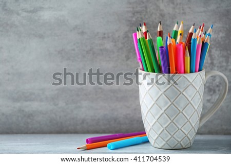 Markers in pencils in ceramic cup in front of wall background