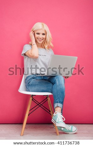 Lovely woman sitting on the chair with laptop computer on pink background