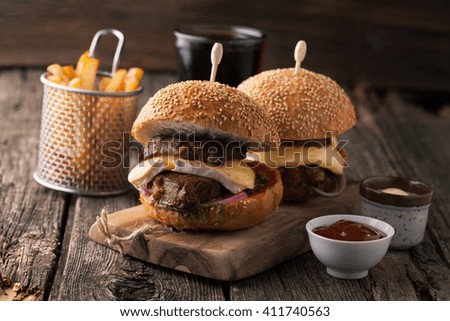 Delicious burger with meat, cheese, lettuce and  french fries on a wooden  background