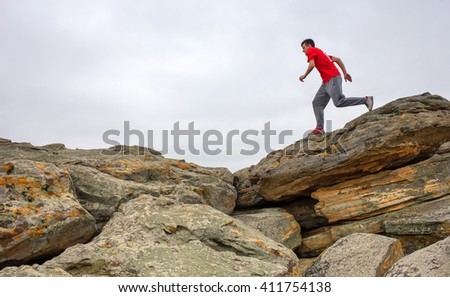 Sport man running, jumping over rocks in mountain area. Fit male runner exercise training and jumping outdoors in beautiful nature