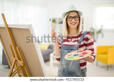 Cheerful female painter posing at home and holding a paintbrush and a color palette