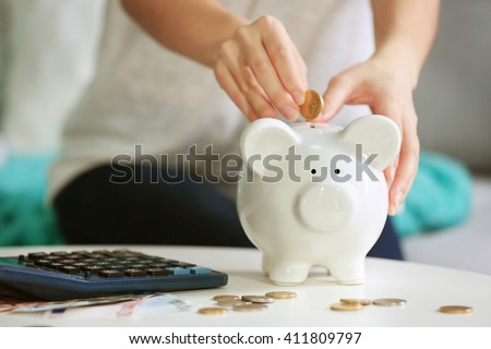 Female hand putting coin into piggy bank closeup Royalty-Free Stock Photo #411809797
