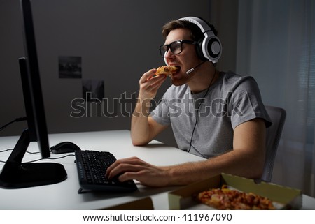 technology, gaming, entertainment, let's play and people concept - young man in headset with pc computer eating pizza while playing game at home and streaming playthrough or walkthrough video Royalty-Free Stock Photo #411967090