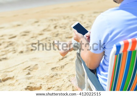 Closeup on man chilling on the beach using smartphone. Back side view of guy enjoying outdoors background