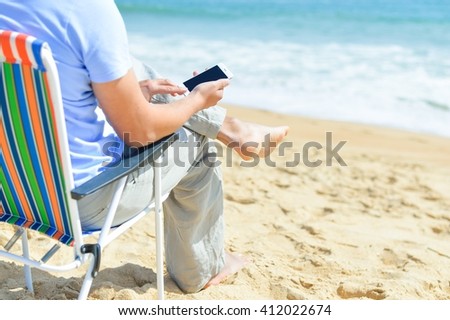 Person chilling on beach talking using smartphone. Back side view of guy enjoying outdoors background