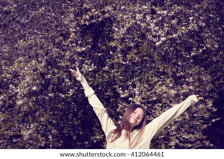 Portrait of girl in front of foliage with arms open making peace sign