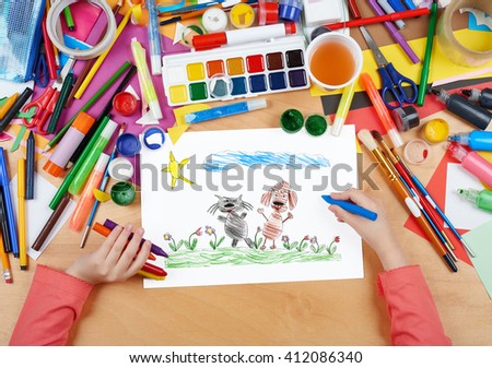 child drawing cat and dog friends walk on grass, top view hands with pencil painting picture on paper, artwork workplace