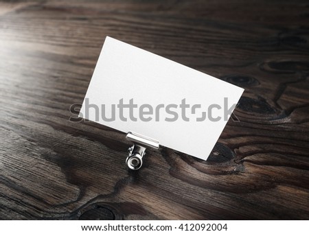Blank white business card in paper clip on dark brown wooden background. Mock-up for branding identity for design presentations and portfolios.