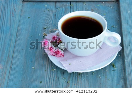Very cute and tender composition with cup of black coffee and little bouquet of pink daisies on blue aged wooden table. Romantic view. Shabby chic