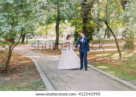 Happy wedding couple charming groom and brunet bride walking holding hands in park