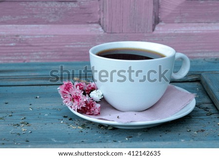 Romantic composition with a very cute white cup of black coffee and little bunch of pink daisies on aged blue table. Vintage. Contrast colors