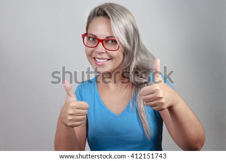 Happy beautiful girl in stylish red glasses showing thumb up symbol by two hands on gray background