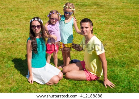 Young family of four sitting on the grass and have fun