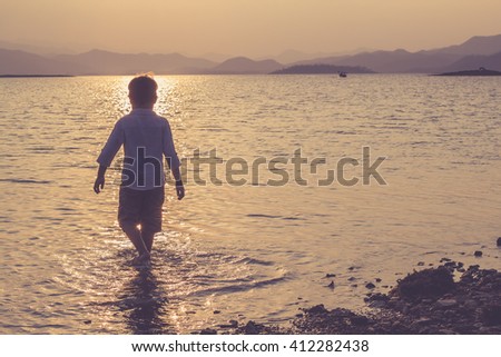 of a Boy Walking into the sea at Sunset / Vintage concept