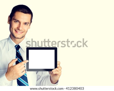 Happy smiling beautiful young businessman showing blank no-name tablet pc monitor, with copyspace area for slogan or text message, with copyspace area, posing at studio