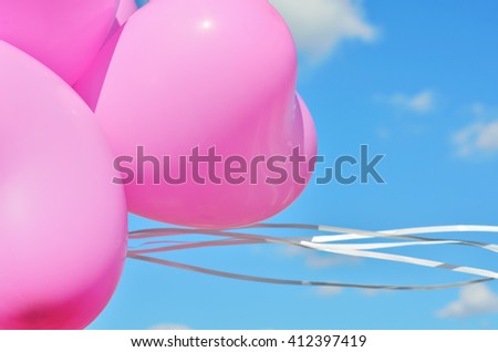Pink balloons with white ribbons close up against the sky