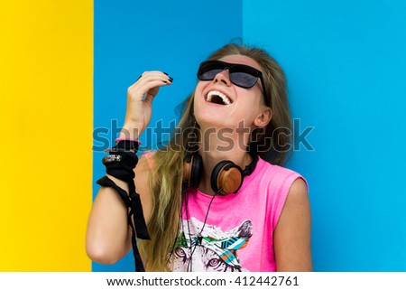 young beautiful blonde girl posing in sunglasses in a pink shirt, on the background of bright walls,with headphones listening to music,doing a selfie make photos of yourself, outdoor portrait,close up