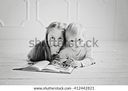 education and school concept - little sisters lying on a floor with a book studying and reading. happy kids boys brothers reading encyclopedia together at home - black and white