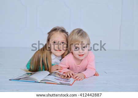 education and school concept - little sisters lying on a floor with a book studying and reading. happy kids boys brothers reading encyclopedia together at home 
