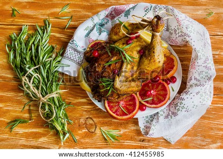 Roasted whole chicken on wooden table. Served with red oranges, lemon, rosemary and cranberries. Top view.