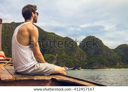 Handsome male cruising on retro wood boat by Andaman sea and behind him you can see Ko Phi Phi Lee Island in full glory. He's turned his back and enjoying the view. 
