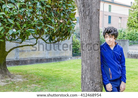 young boy smiles leaning against the trunk of a catalpa tree in garden