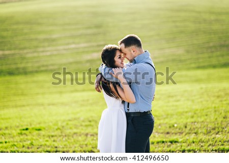 Stylish guy with suspenders and a pretty girl in a white dress walking on the field on a background of green grass