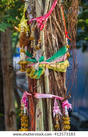 Strips of different colored fabric ribbons decorate a  tree near a Buddhist temple 