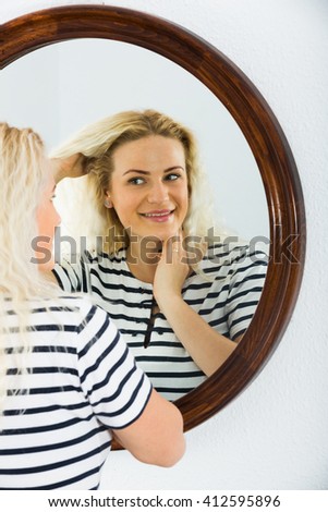 Portrait of long haired blondie checking her skin in mirror