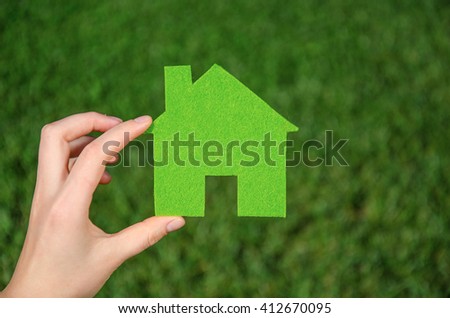 Hand holding eco house icon concept on the green grass background