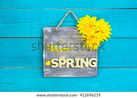 Welcome SPRING sign with yellow spring flowers hanging on antique rustic teal blue wooden background; Mothers Day and springtime floral background with painted wood copy space
