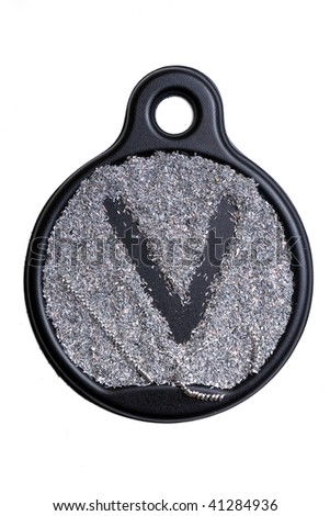 The letter "V" formed on a black plastic detail by shiny metal sawdust. Isolated object.