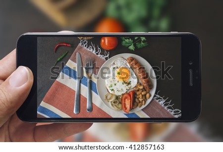 Taking picture of fried eggs and tomato with mobile phone in male hands. Vintage style. Top view.