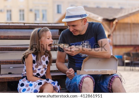 happy father and daughter eating pizza outdoor