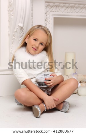 Cute little blond girl sitting with a gift near fire-place