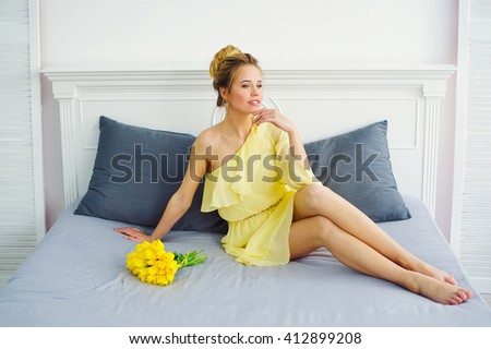Beautiful young woman in yellow dress posing with bunch of fresh tulips on her bed