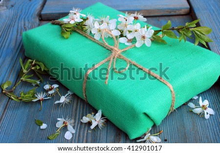 Simple gift box wrapped with green linen cloth and jute decorated with branch of cherry tree with white spring flowers. Handmade.