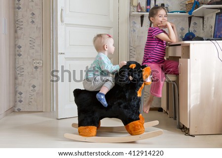 Children playing at home as usual. Five year old girl watching cartoons on the notebook, and her kid sister swinging on a rocking horse