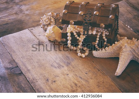 image of white pearls necklace in treasure chest next to seashells on old grunge wooden table. vintage filtered and toned
