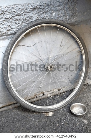 Bicycle wheel is leaning against a gray textured wall. Poverty.