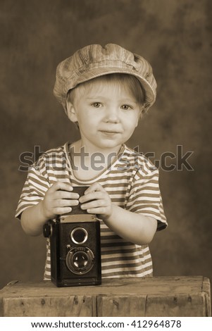 Young blond boy holding retro twin-lens reflex camera in photo studio, photographer, sepia tone