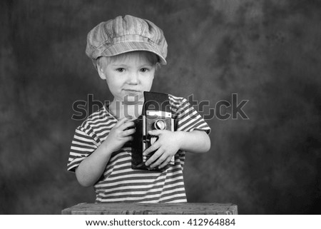 Young blond boy holding retro twin-lens reflex camera in photo studio, photographer, black and white photo