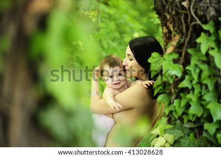 Baby and mother hugging kissing topless portrait outdoor summer nature on blurred green background, horizontal picture