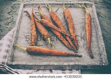 Glazed and roasted young red carrots on a piece of a quartz stone plate on grey Background ,  baked  baby carrots in  Horizontal overhead view. Amazing unique post-production photo 