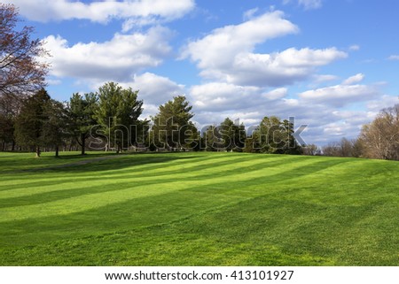 Green field and blue sky. Spring background. Spring nature wallpaper. Open golf course field. Puffy clouds with trees and green field