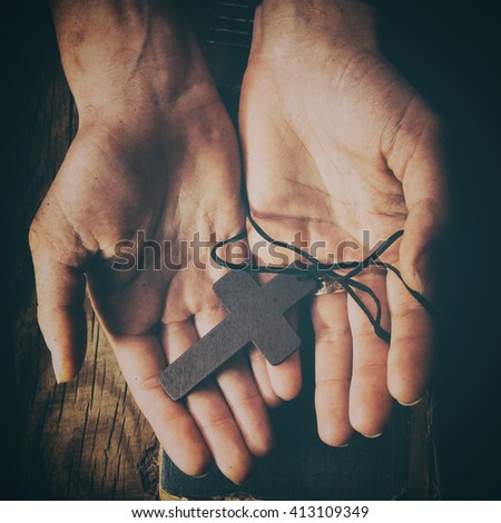 closeup of hands holding vintage cross on Bible