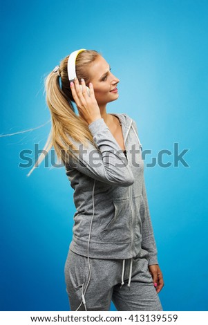 Portrait of young blonde woman in sportswear listening to music with cell phone.Studio shot. Blue background. Isolated.
