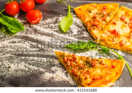 slices of pizza on the black background of cherry tomatoes